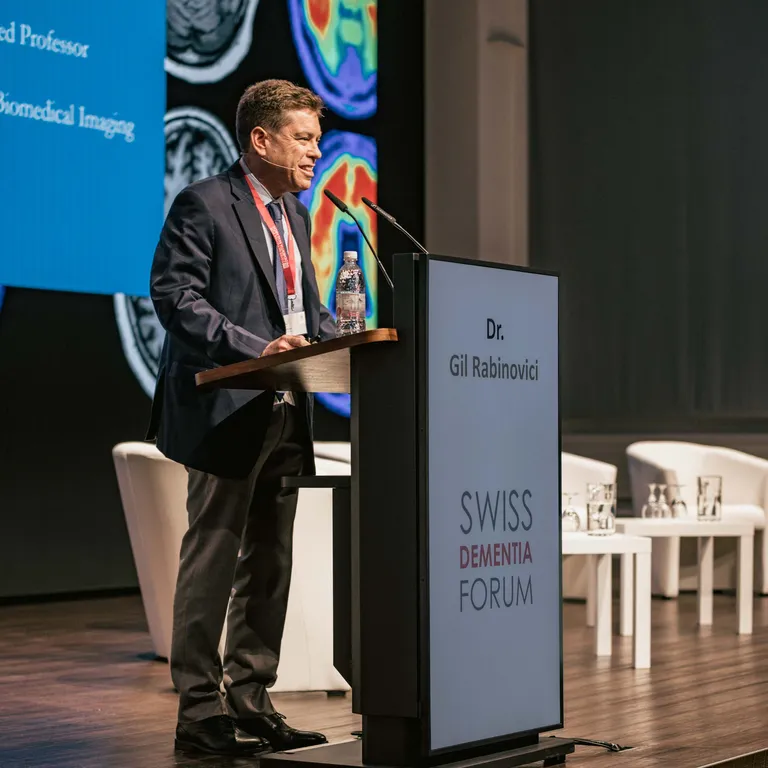 A man named Gil Rabovinovici stands on stage behind the lectern.