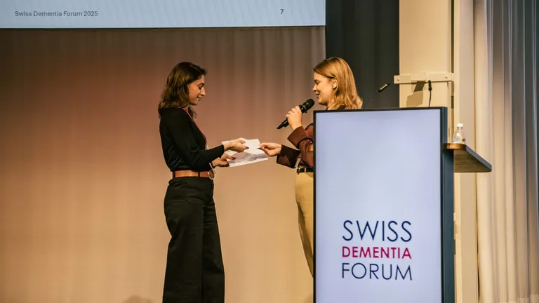 Two women are standing on stage, one is presenting the other with an award.